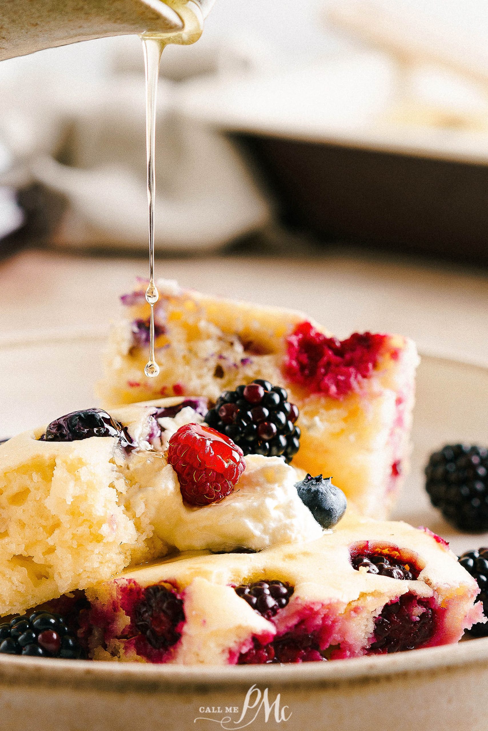 A slice of sheet pan pancakes with berries being drizzled with honey.