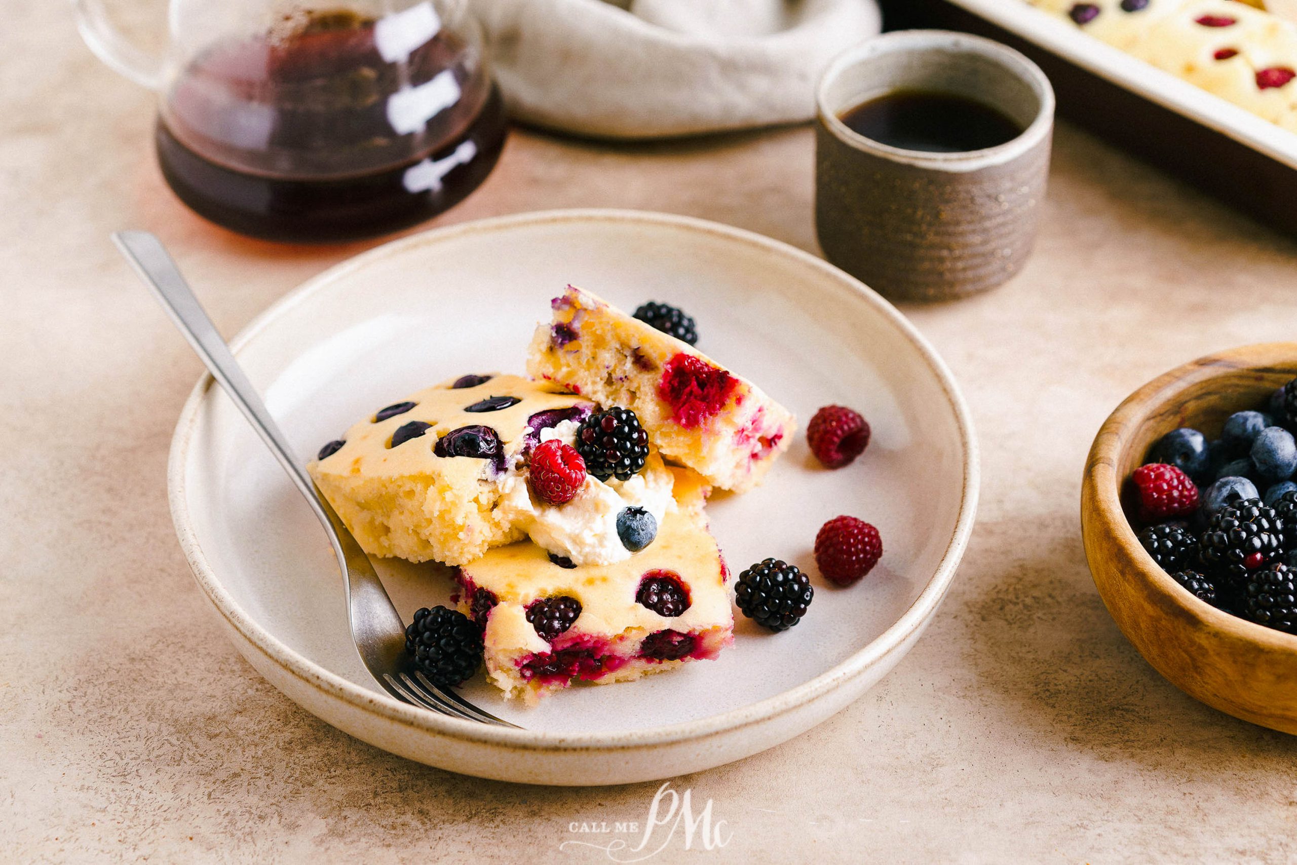 A plate of berry pancakes with berries and a cup of coffee.
