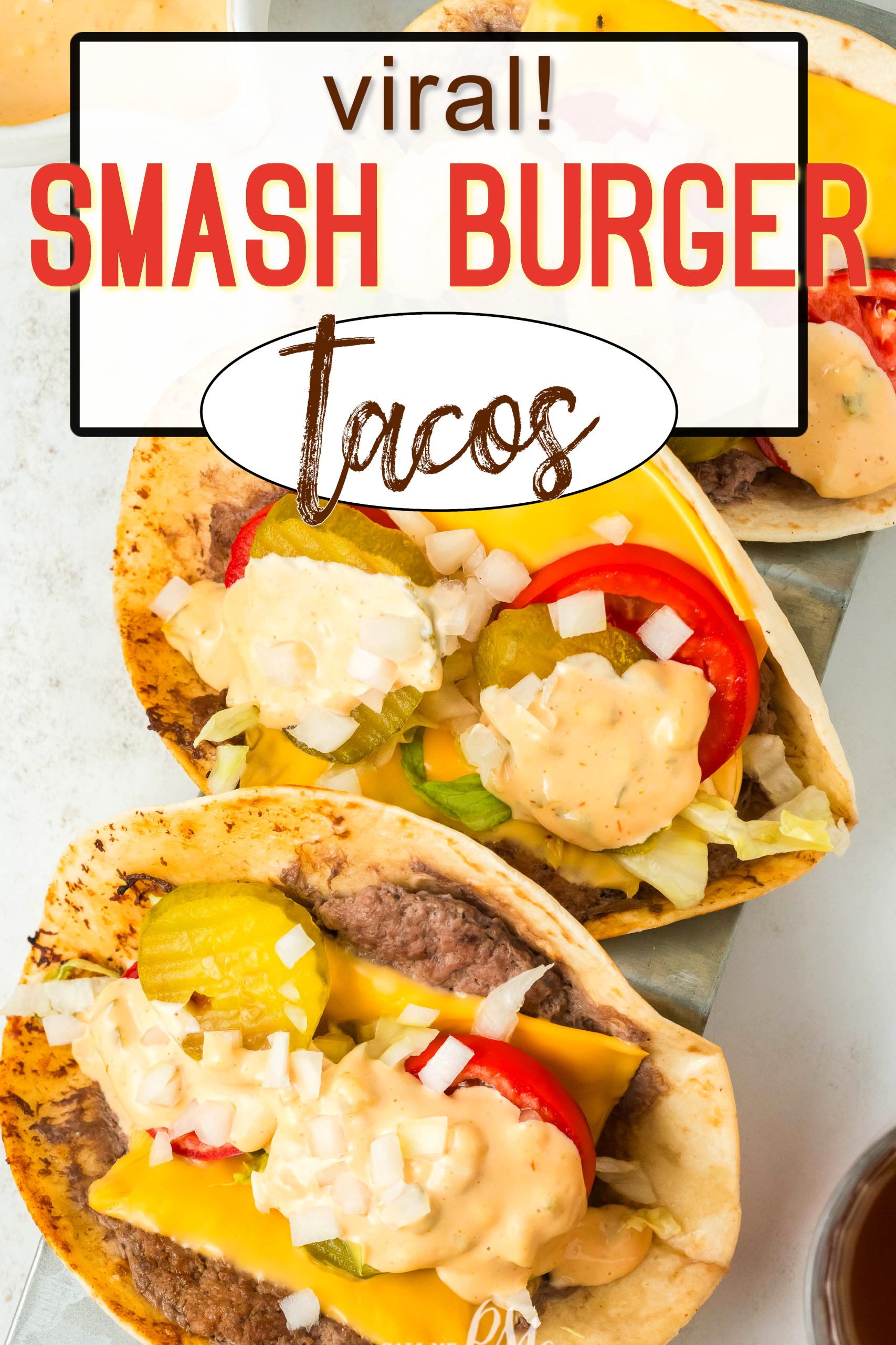 Three Viral Smash Burger Tacos on tortillas, topped with cheddar cheese, pickles, onions, lettuce, tomato, and sauce, arranged on a white surface. Text at top reads "Viral! Smash Burger Tacos.