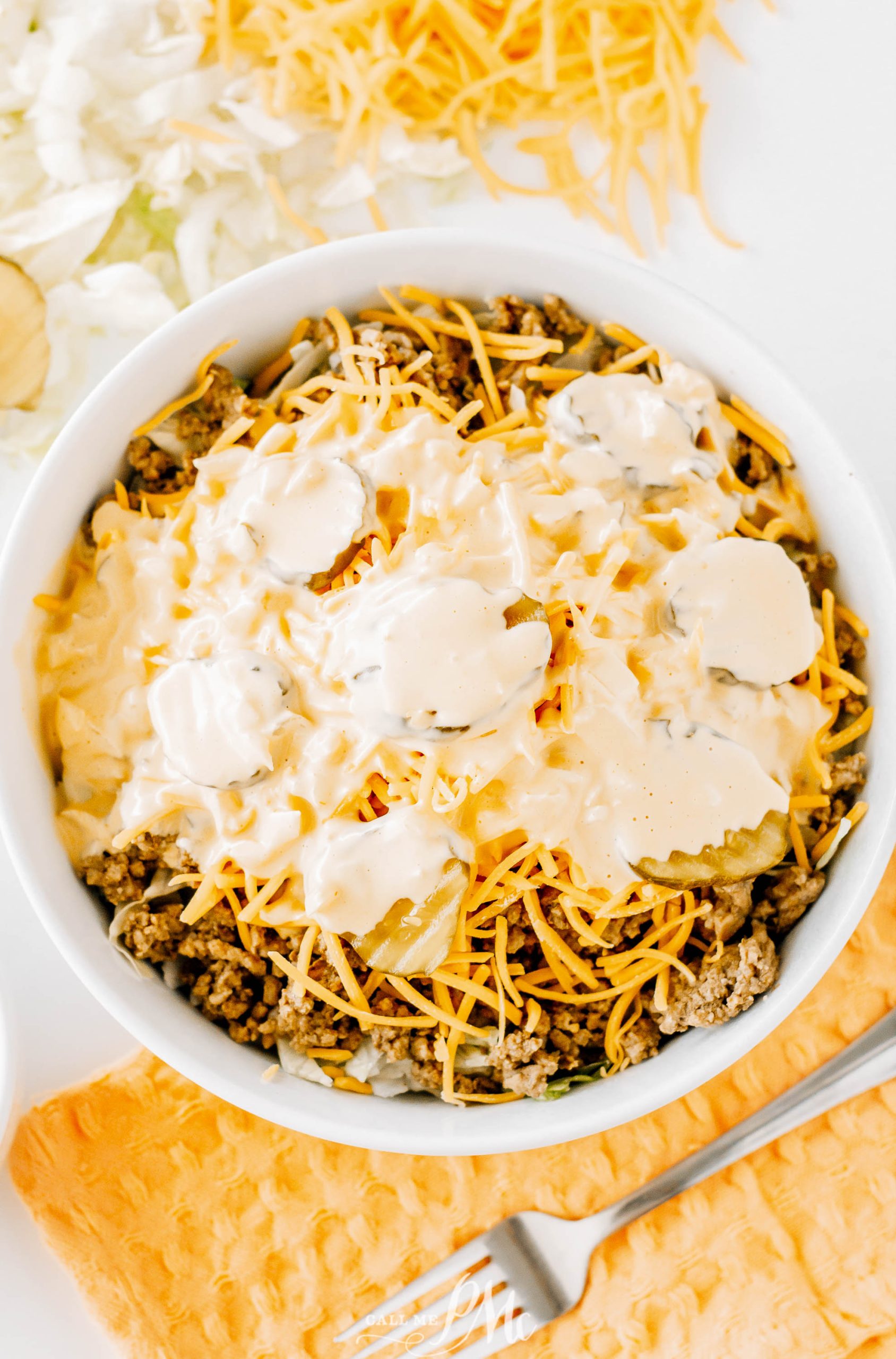 Cheesy nachos in a white bowl with shredded cheese.