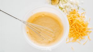 A bowl of cheese sauce with a whisk in it.