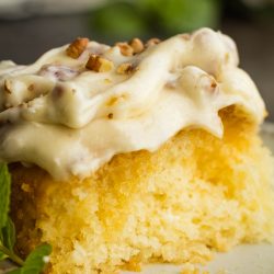 A slice of Elvis Presley Pineapple Poke Cake with icing and mint leaves on a plate.