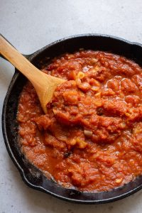 A skillet full of tomato sauce with a wooden spoon.