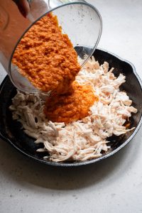 A person pouring a sauce over chicken in a skillet.