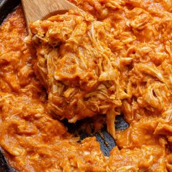 Shredded chicken in a skillet with a wooden spoon.