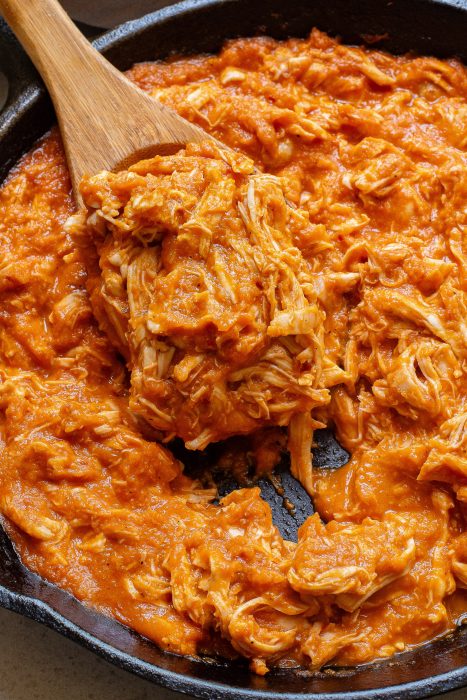 Shredded chicken in a skillet with a wooden spoon.