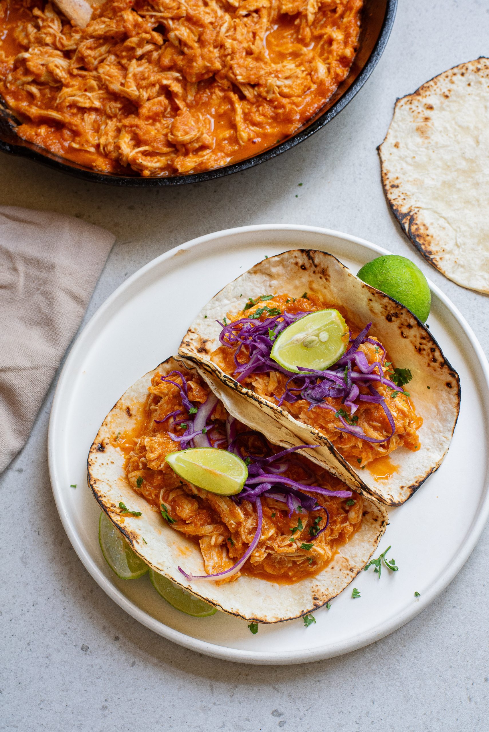 Mexican chicken tinga tacos on a plate next to a skillet.
