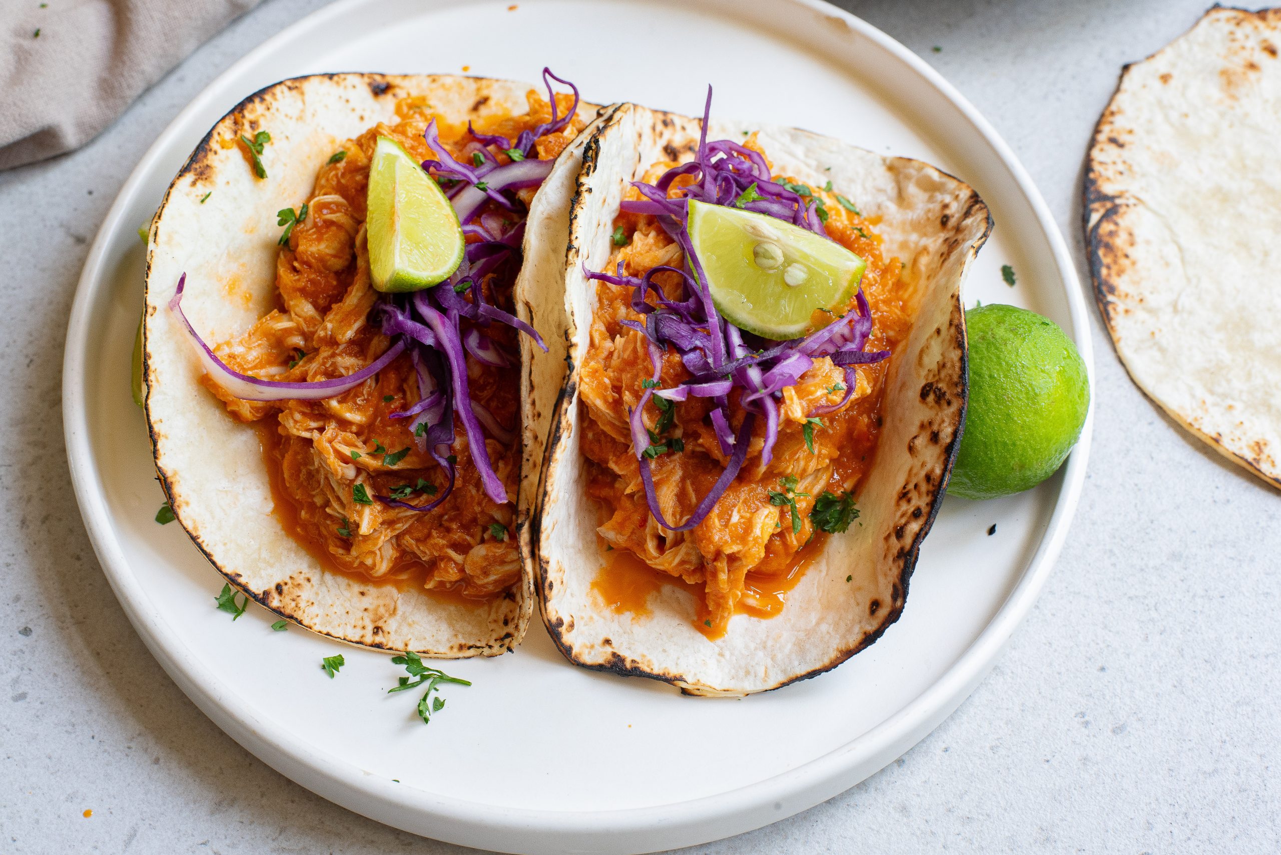 Two Chicken Tinga tacos on a plate with slaw and limes.