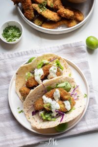 Oven-fried avocado tacos with sour cream and lime on a white plate.