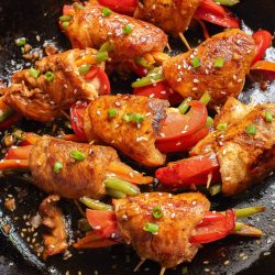 Chicken skewers in a skillet with peppers and onions.