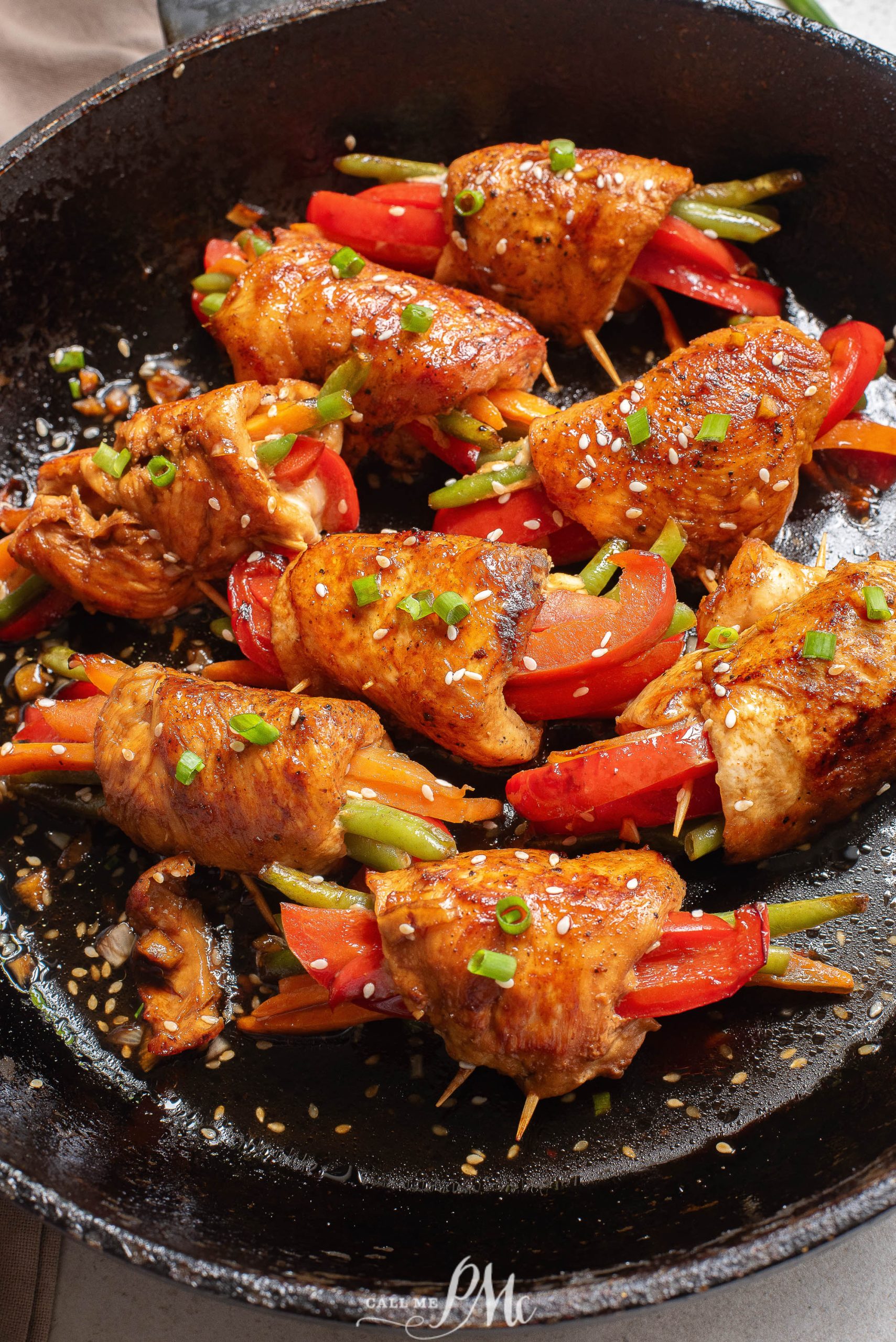 Chicken skewers in a skillet with peppers and onions.