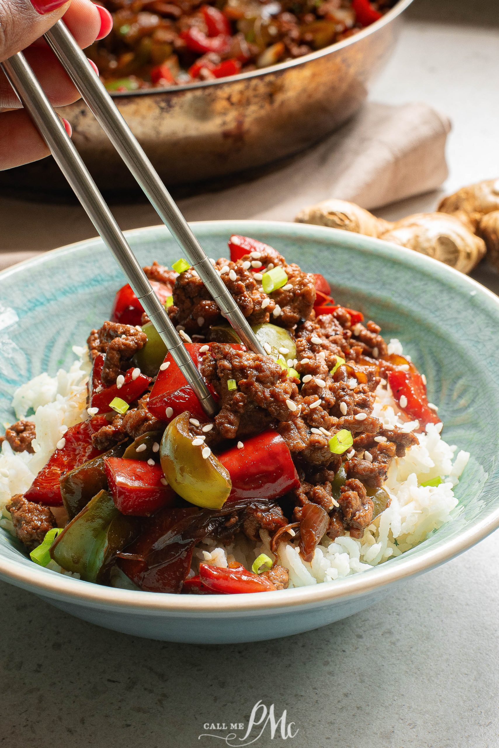 A person holding chopsticks over a bowl of beef stir fry.