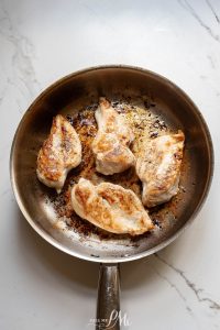Chicken breasts in a frying pan on a marble countertop.