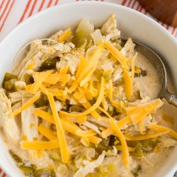 Chicken enchilada soup in a bowl with cheese and green onions.