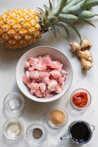 A bowl of chicken, pineapple, ginger, and other ingredients.