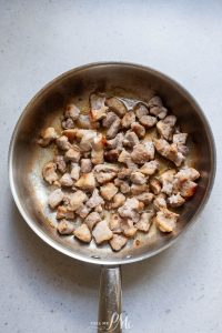Chicken in a frying pan on a white surface.