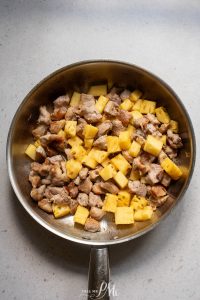 A frying pan filled with meat and pineapples.