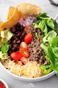 A bowl of mexican salad with meat, lettuce, tomatoes and tortillas.