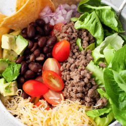 A bowl of mexican salad with meat, lettuce, tomatoes and tortillas.