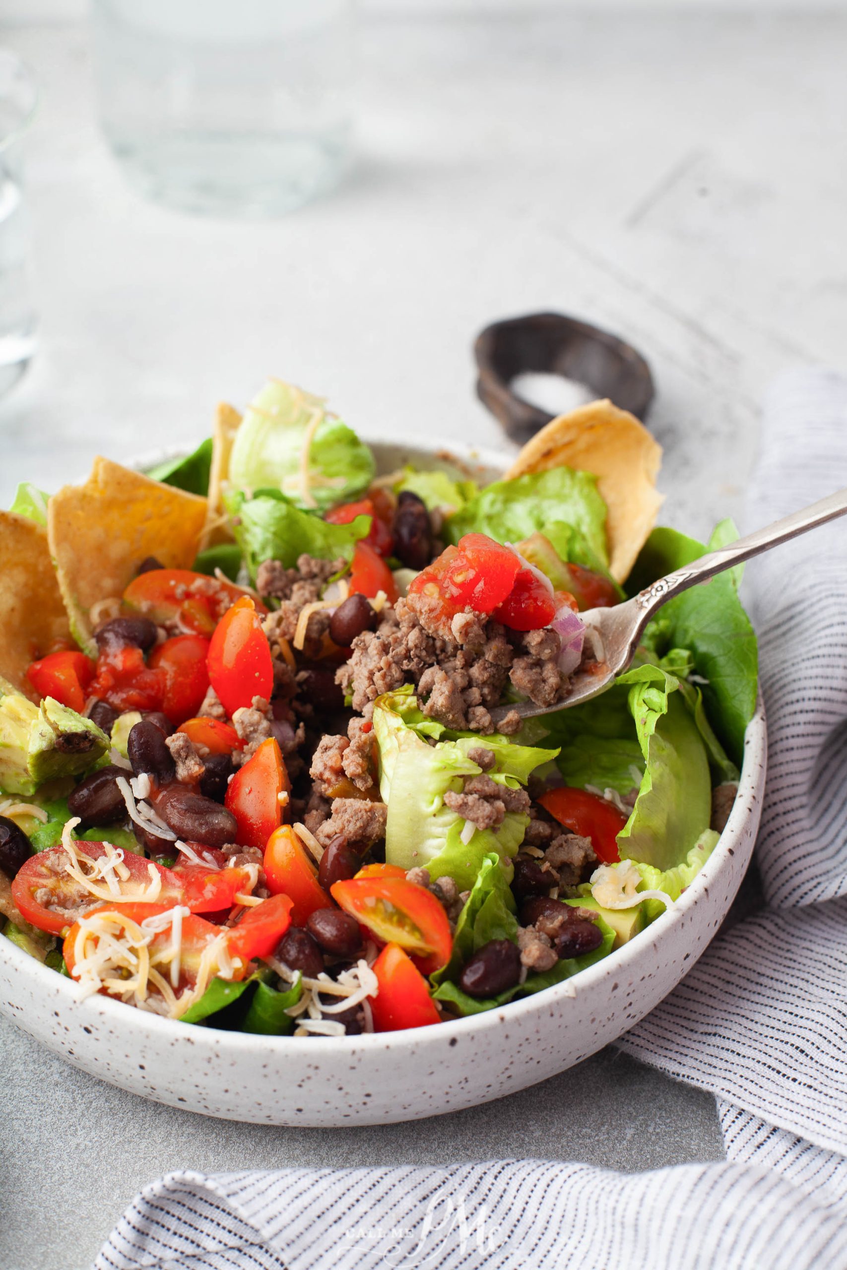 A bowl of salad with meat, tomatoes, lettuce and tortilla chips.