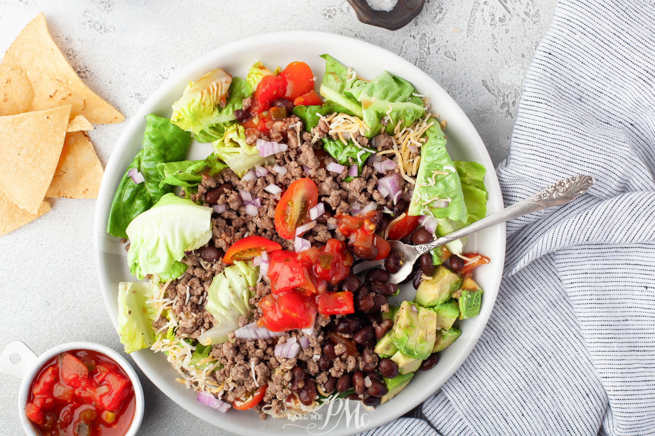 A bowl of mexican salad with beans, tomatoes and tortillas.