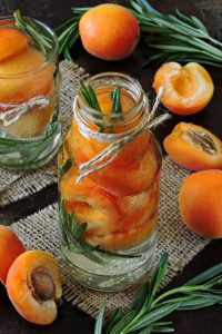 Fresh apricots in jars with sprigs of rosemary.
