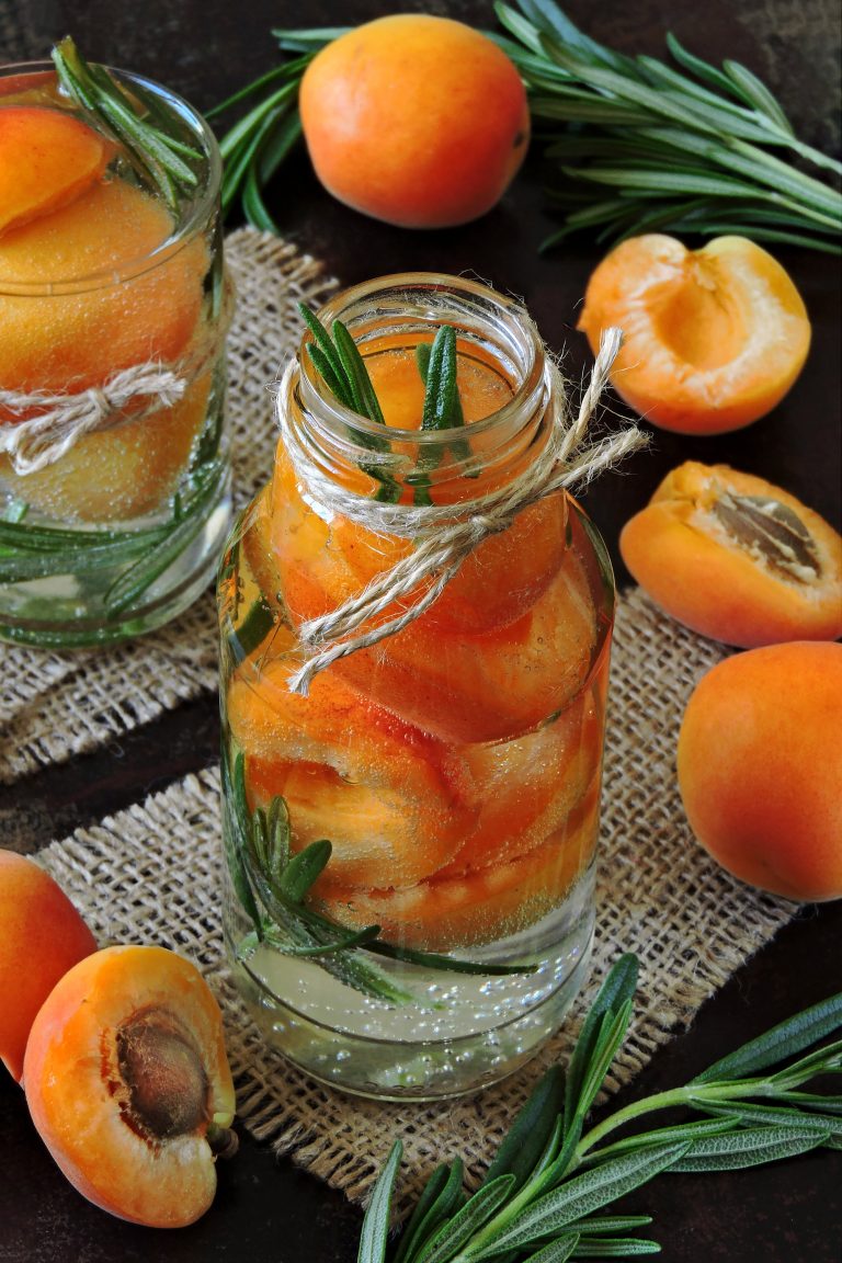 Fresh apricots in jars with sprigs of rosemary.