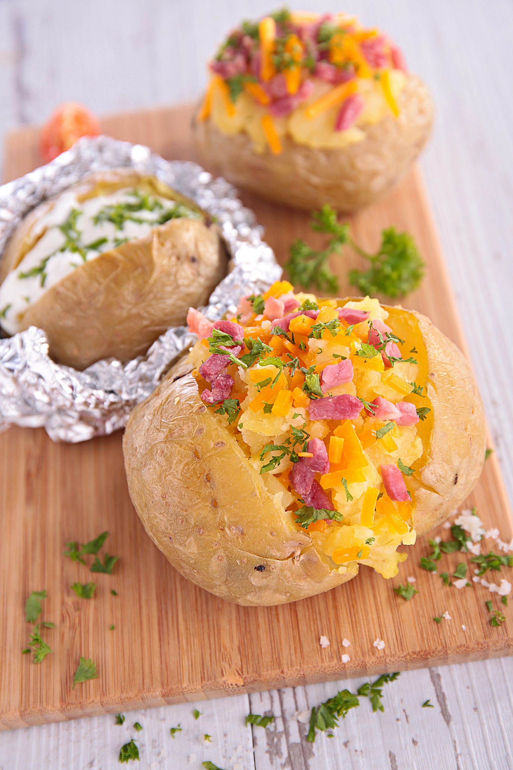 Three stuffed potatoes on a cutting board at a potato bar.