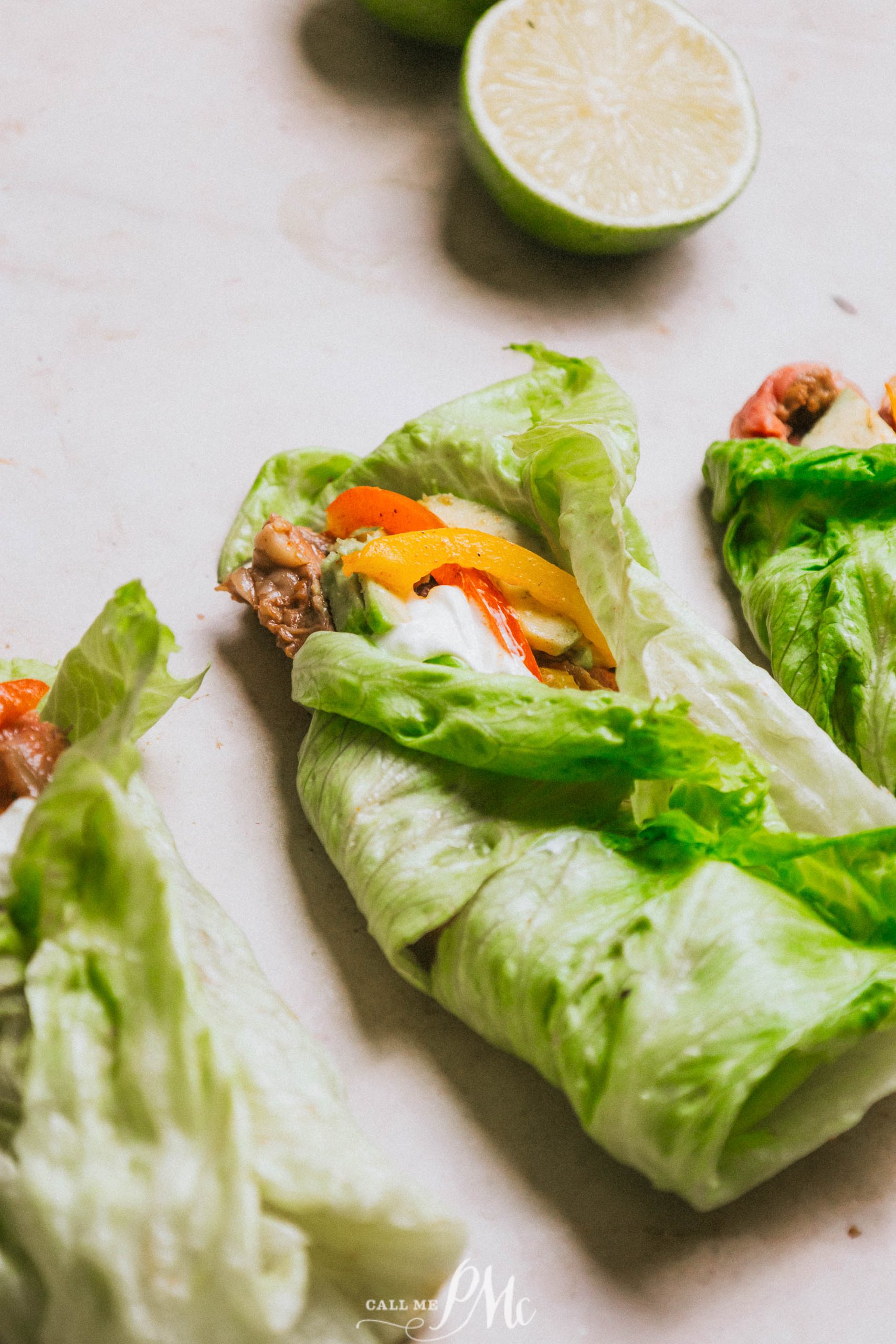 Four lettuce wraps on a table with lime wedges.