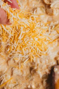 A person holding cheese over a bowl of food.