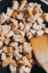 Chicken in a frying pan with a wooden spoon.