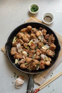 Fried chicken in a skillet with onions and garlic.
