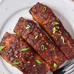 A plate with three pieces of grilled salmon on it.