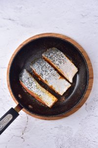 Fried salmon fillets in a frying pan on a white background.