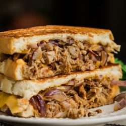 A grilled sandwich with pulled pork and onions on a plate.