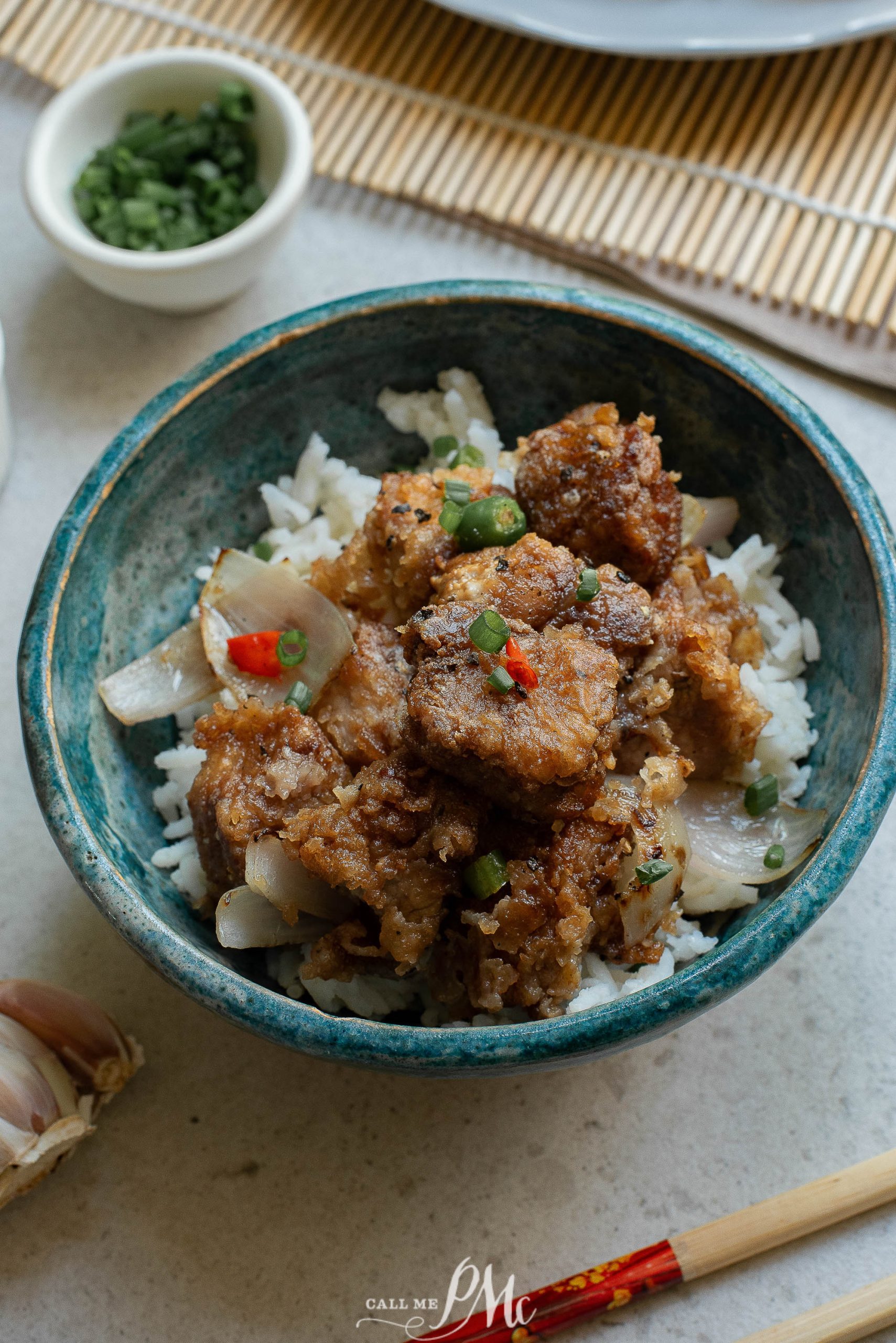 A bowl of meat and rice with chopsticks.