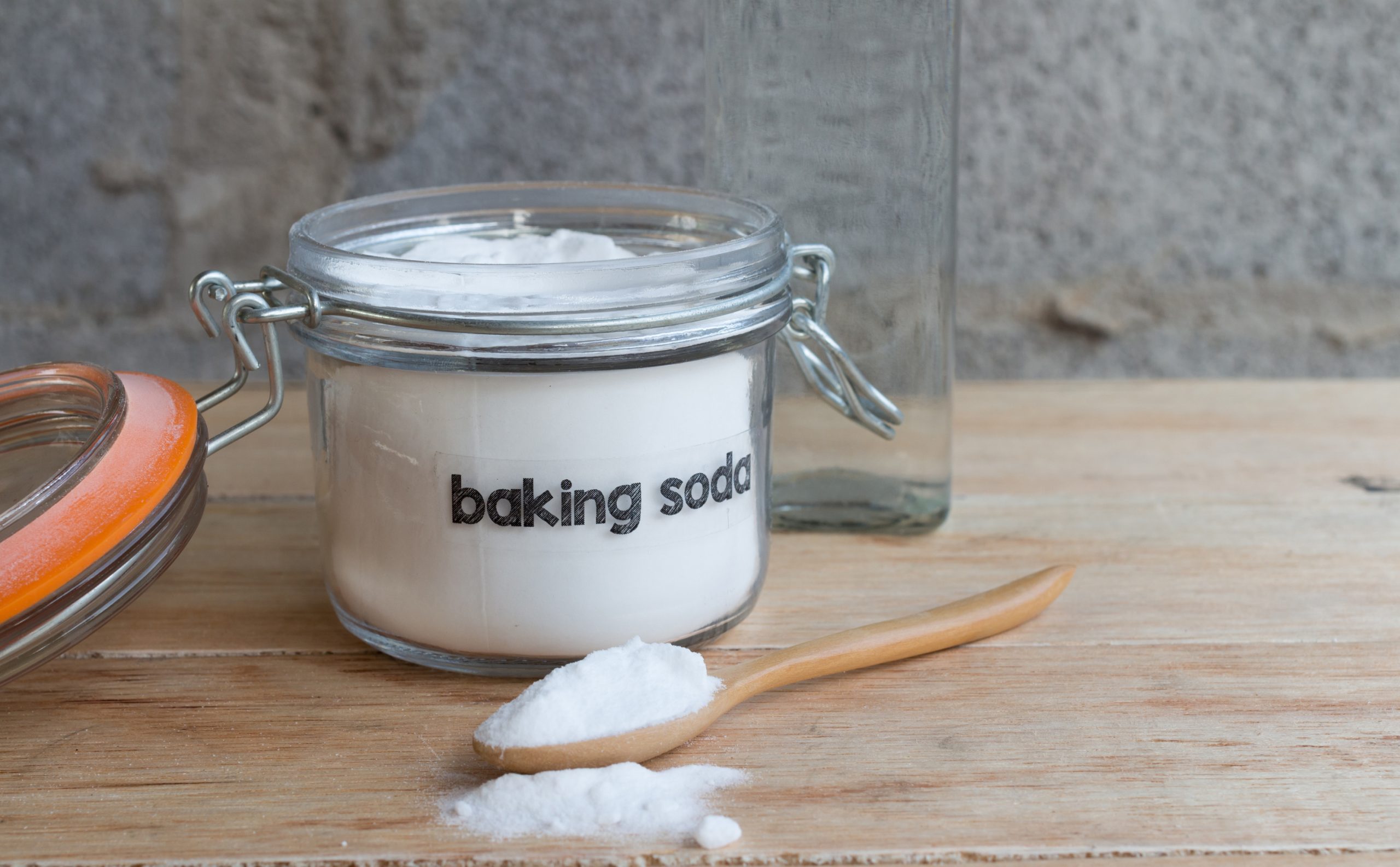 Baking soda in a jar next to a wooden spoon.