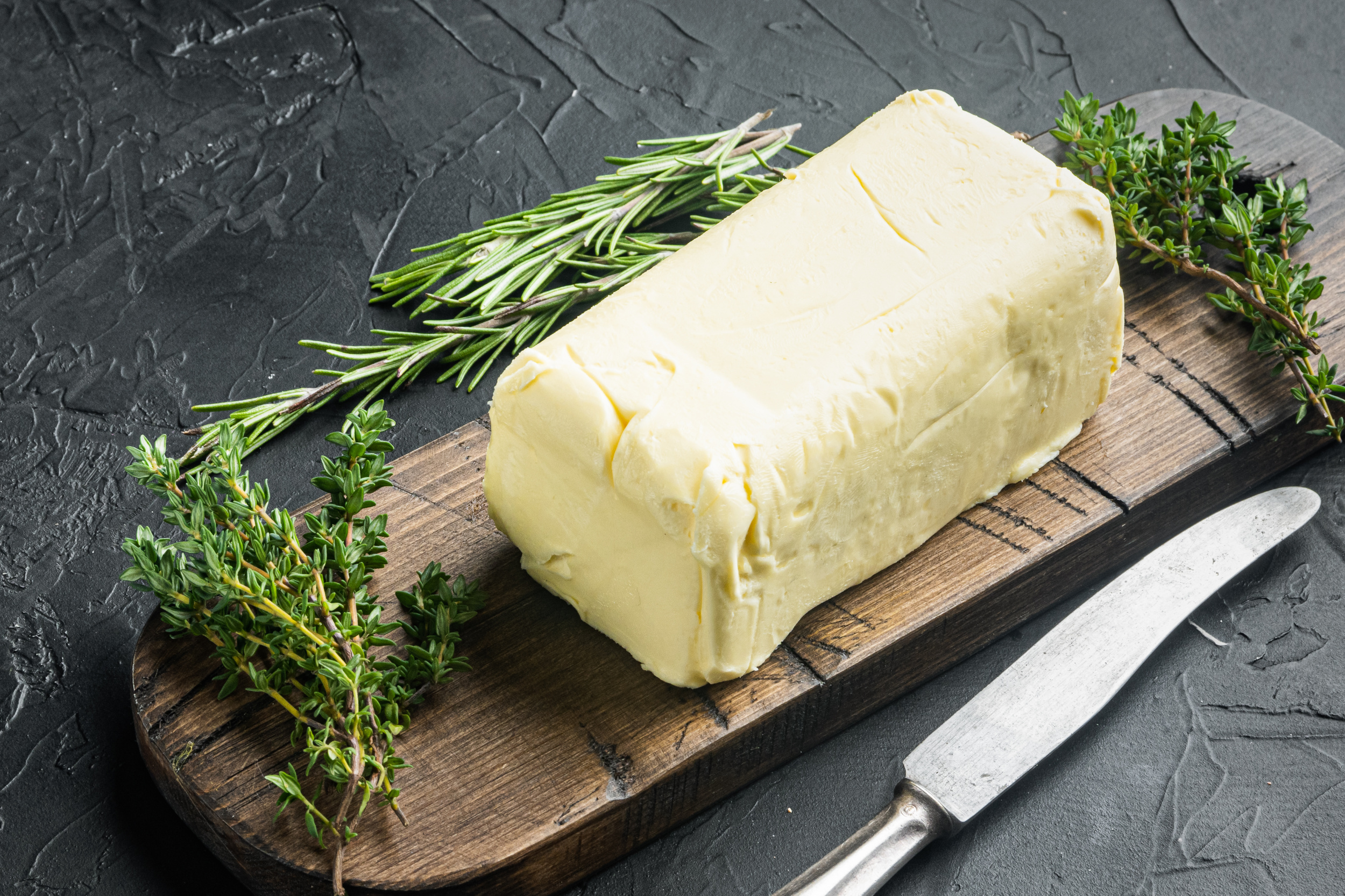 A block of butter on a wooden board next to a knife.