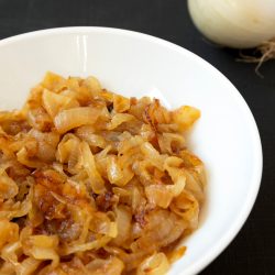 A bowl of onions on a table next to an onion.