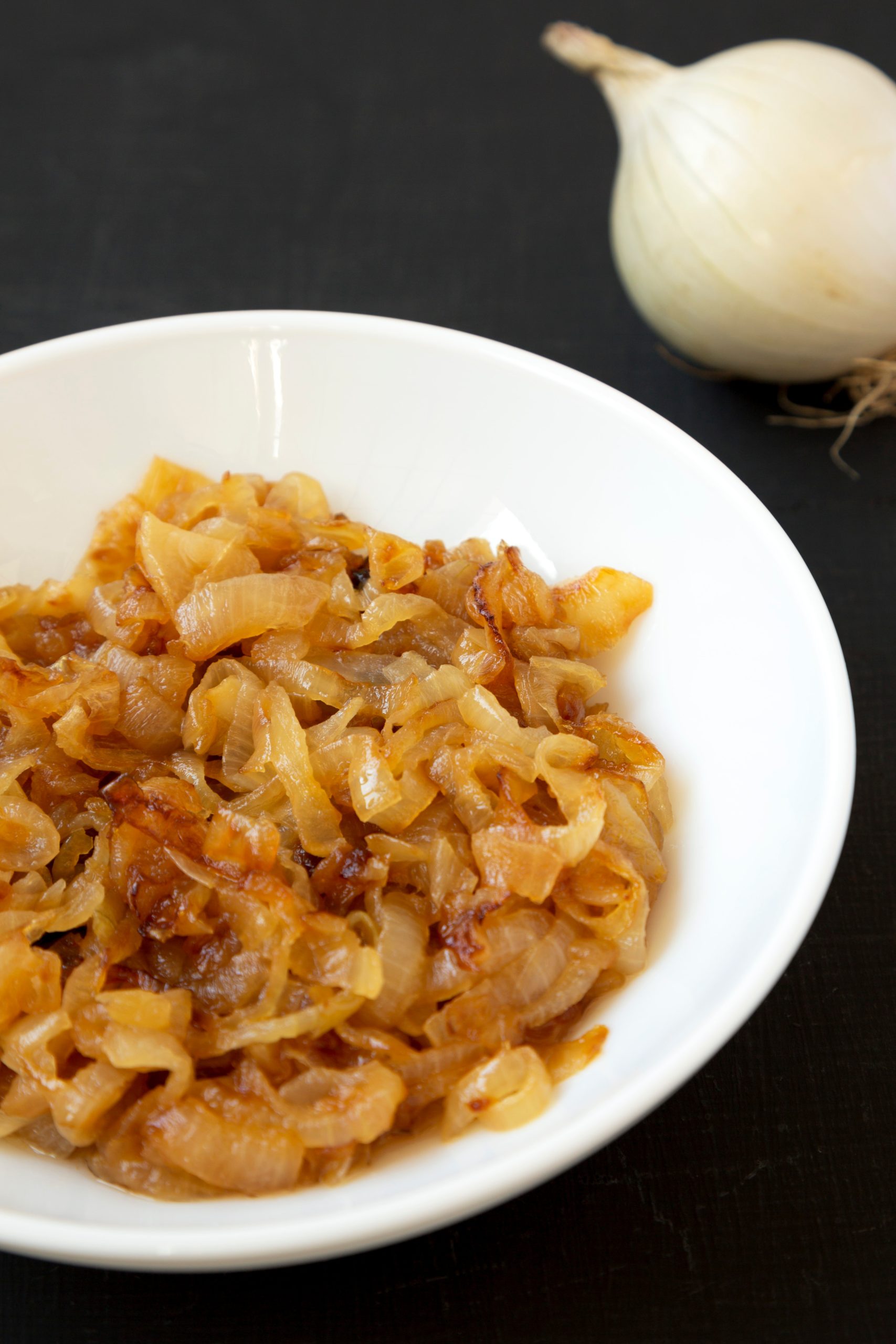 A bowl of Caramelized Onions Recipe on a table next to an onion.