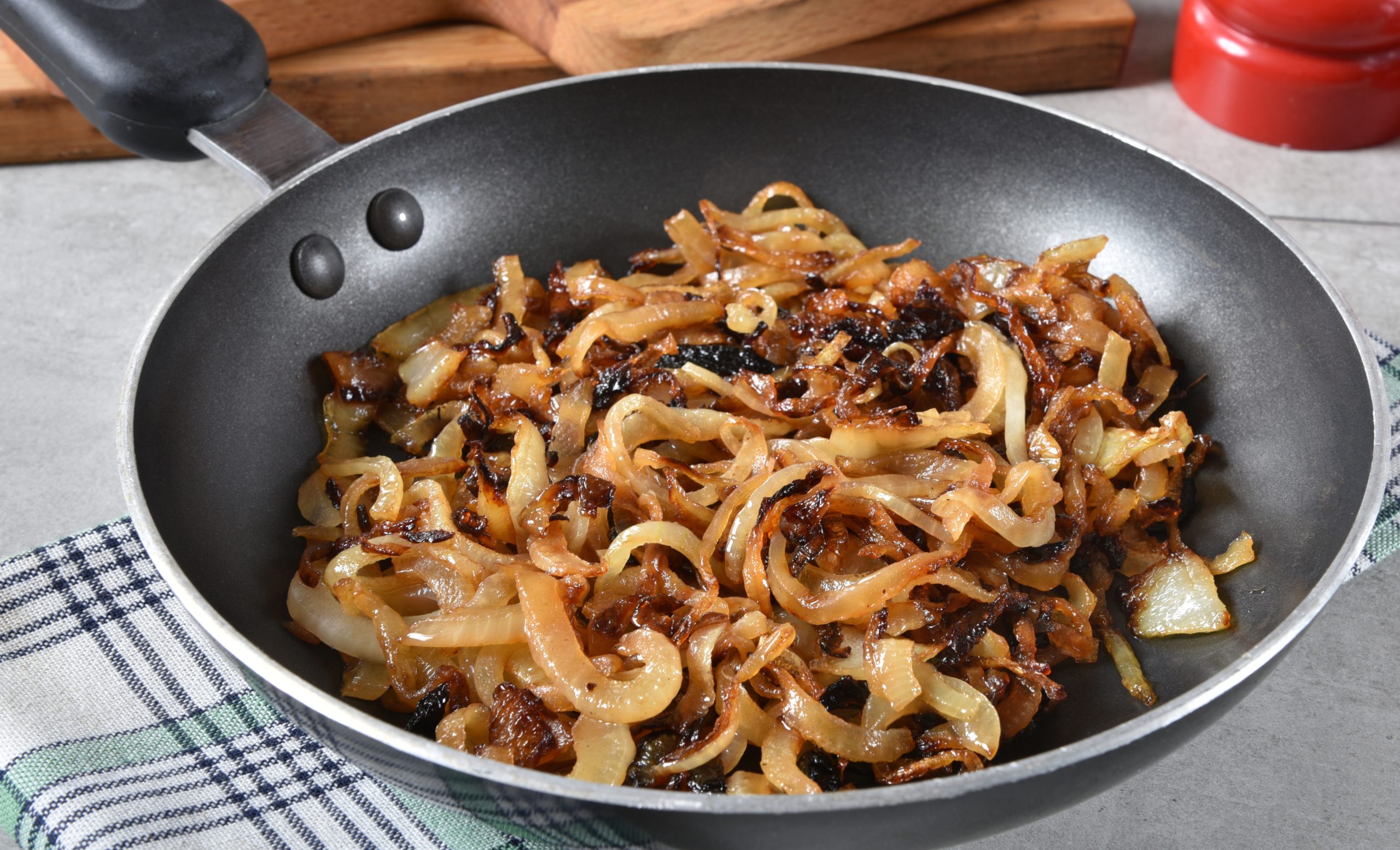 Caramelized Onions Recipe in a frying pan with a wooden spoon.