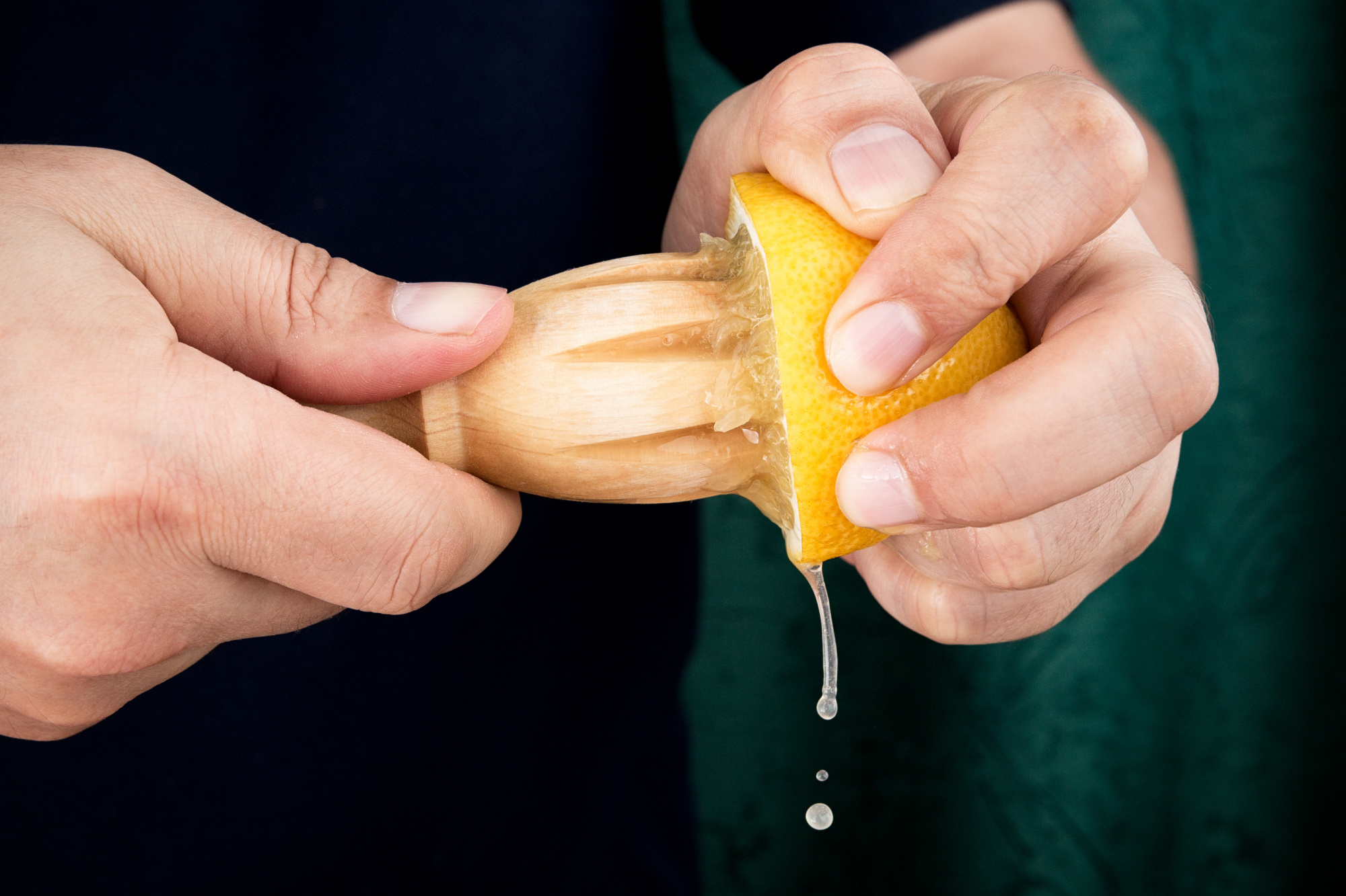 A person squeezing a lemon with a wooden spoon.