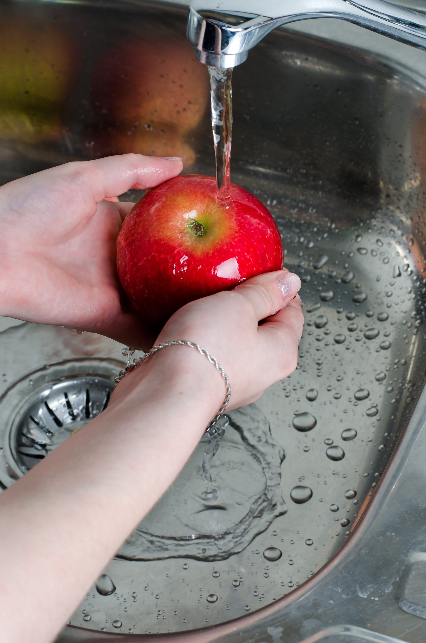 A person washing an apple in a sink.