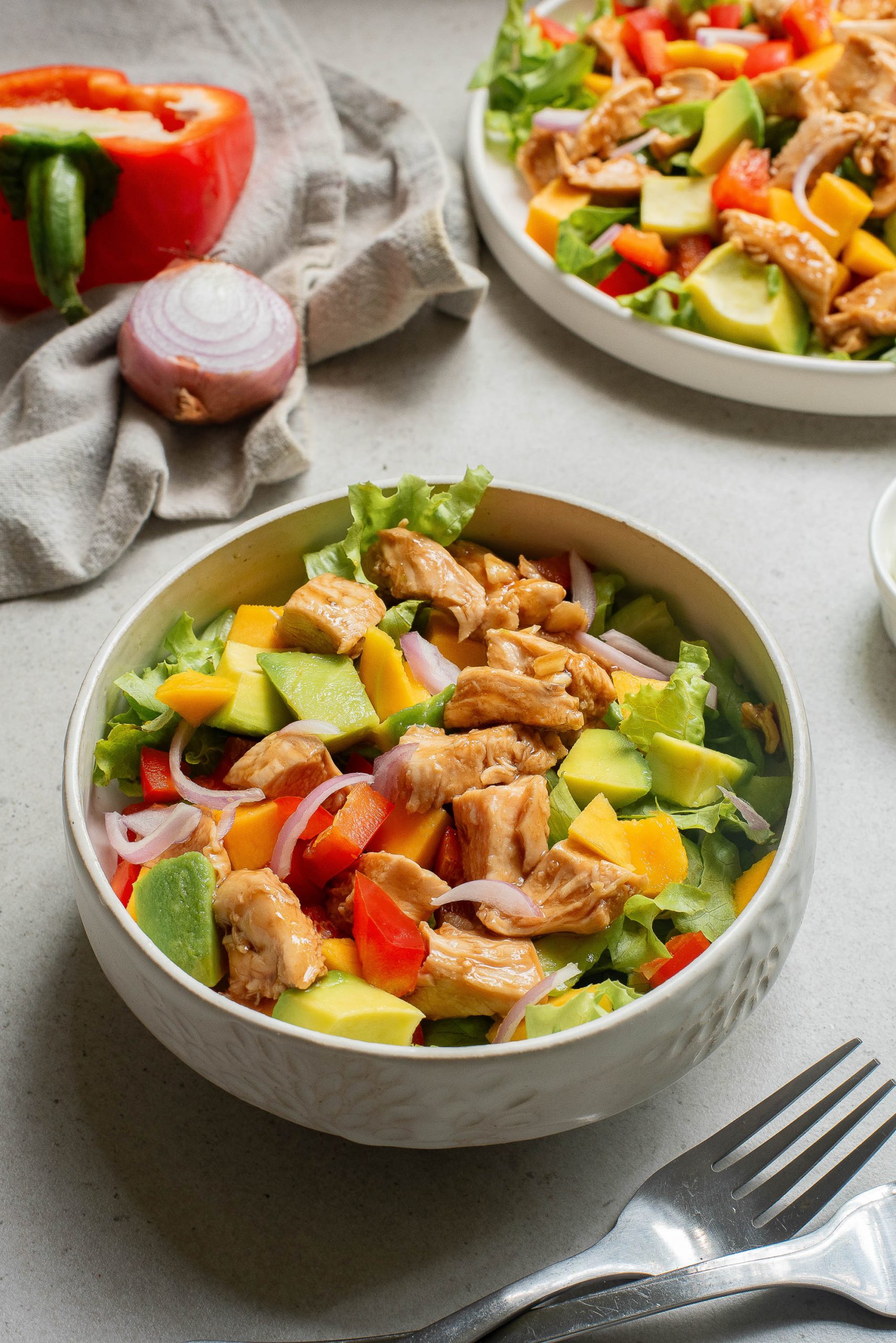 Two bowls of Hot Honey Garlic Chicken Salad with avocado, tomatoes and peppers.
