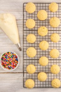 Cupcakes on a cooling rack next to a bowl of sprinkles.