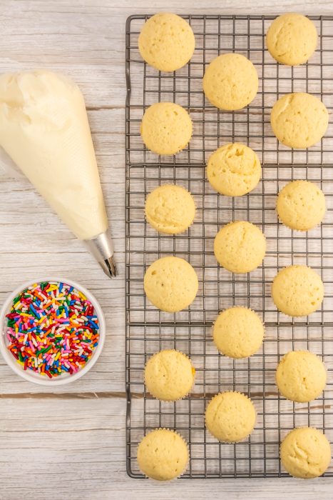 Vanilla Cupcake on a cooling rack next to a bowl of sprinkles.