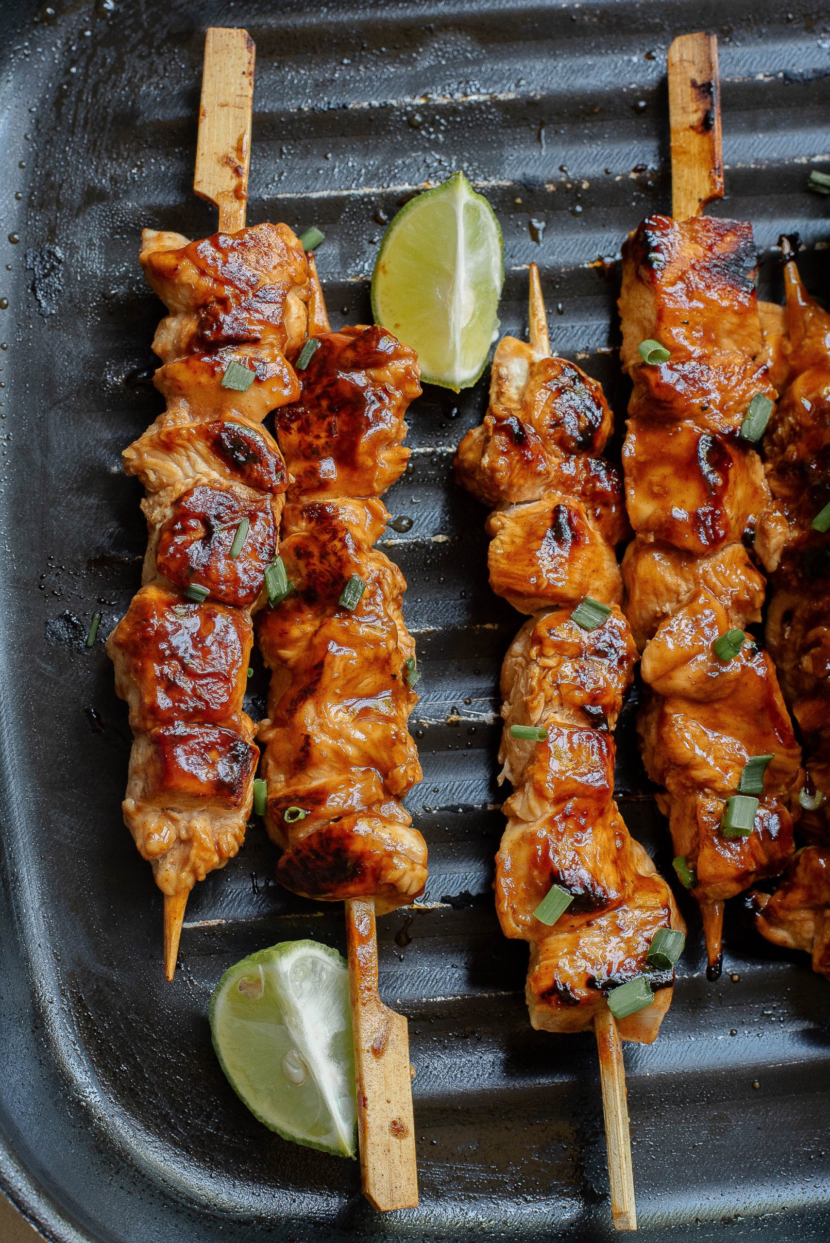 Chicken skewers on skewers with lime wedges.