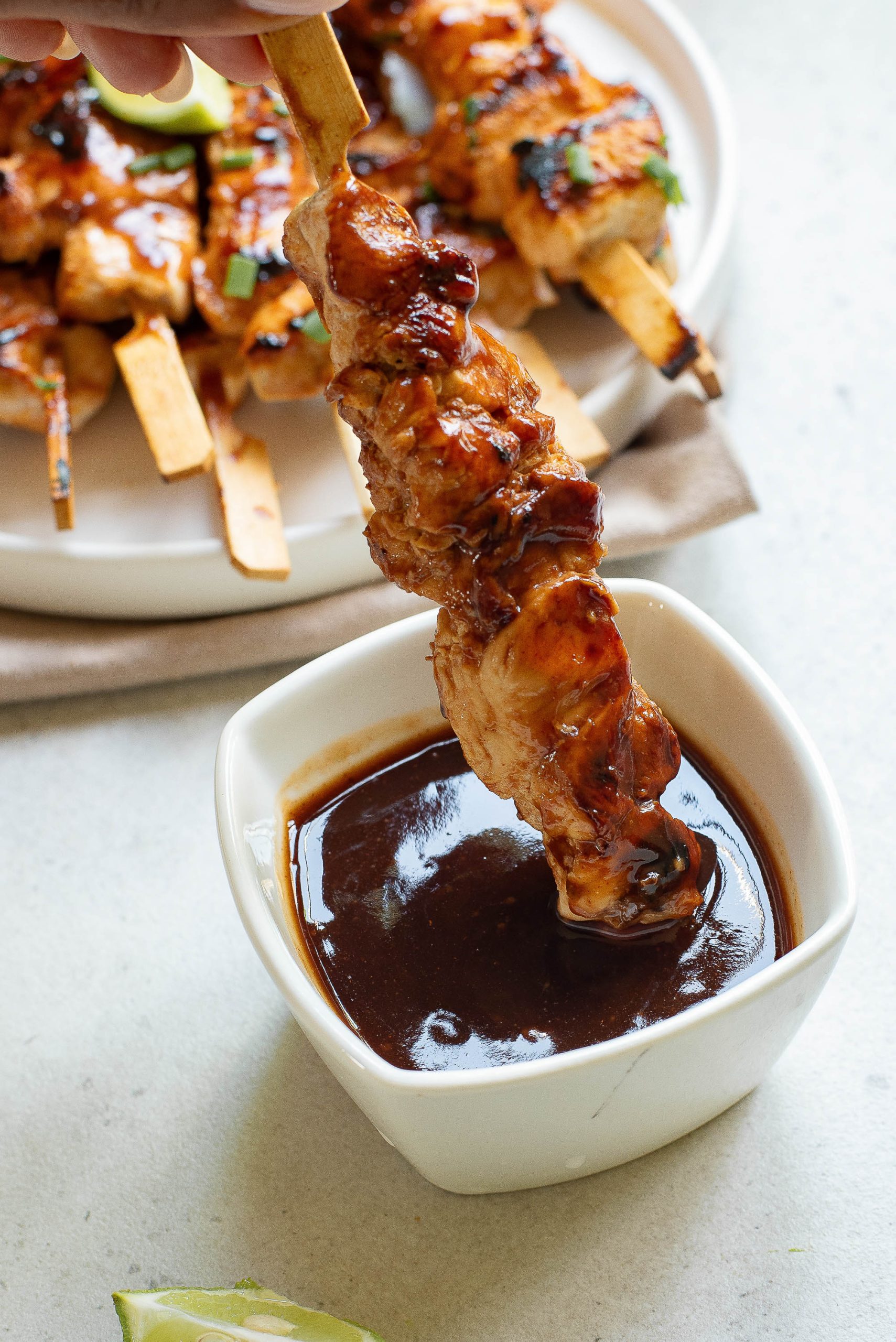 A person is dipping chicken skewers in a sauce.
