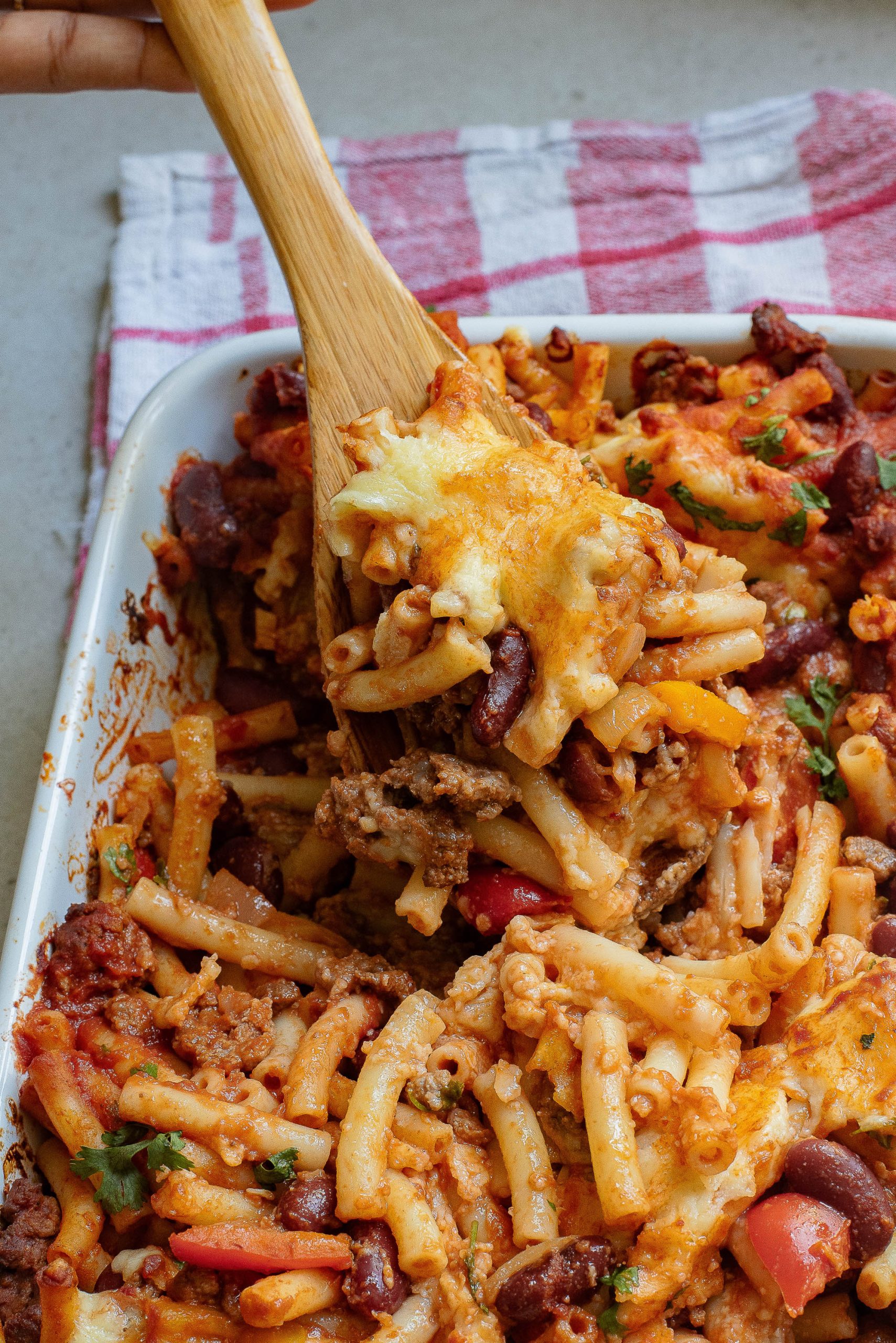 A wooden spoon is being used to scoop pasta out of a baking dish.