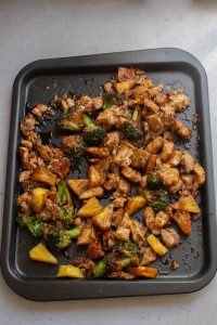 A black pan with chicken and vegetables on it.